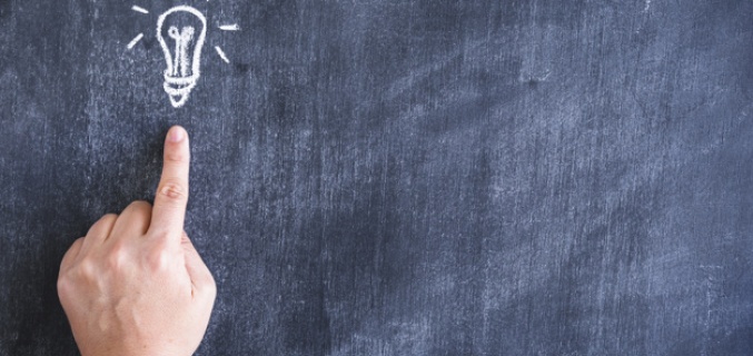 Finger points to a painted light bulb on a blackboard