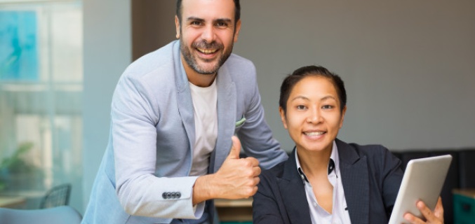 Two colleagues laugh into the camera at their workplace.